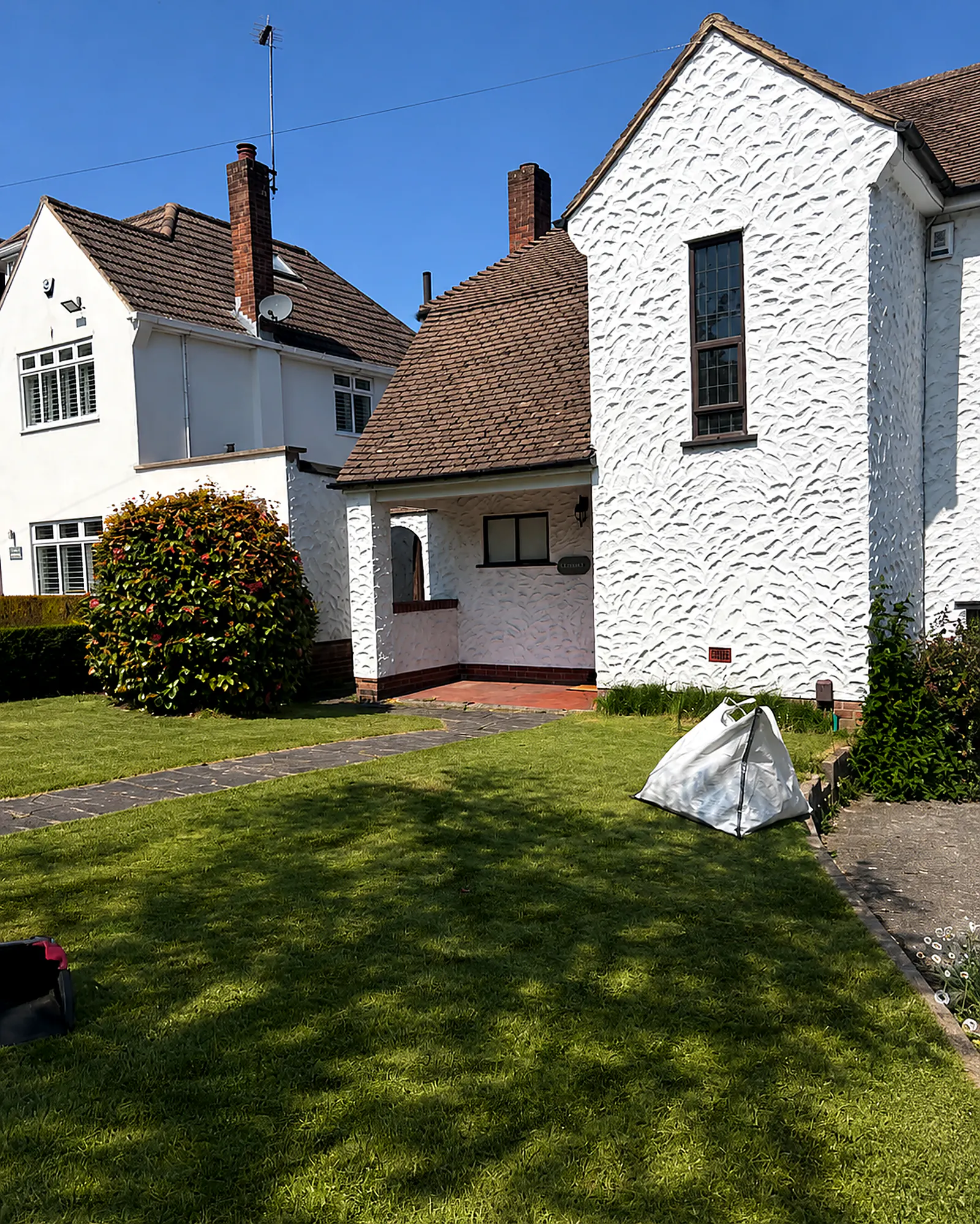 A neat front lawn beside a pebbledash render house, mid-job with a Vertglows green-waste bag set on the path